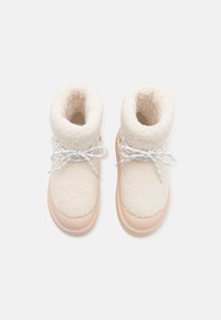 Bottes avec une tige en textile crème et duveteux et une semelle en caoutchouc pêche clair, présentant des lacets blancs et un design retroussé pour plus de chaleur.