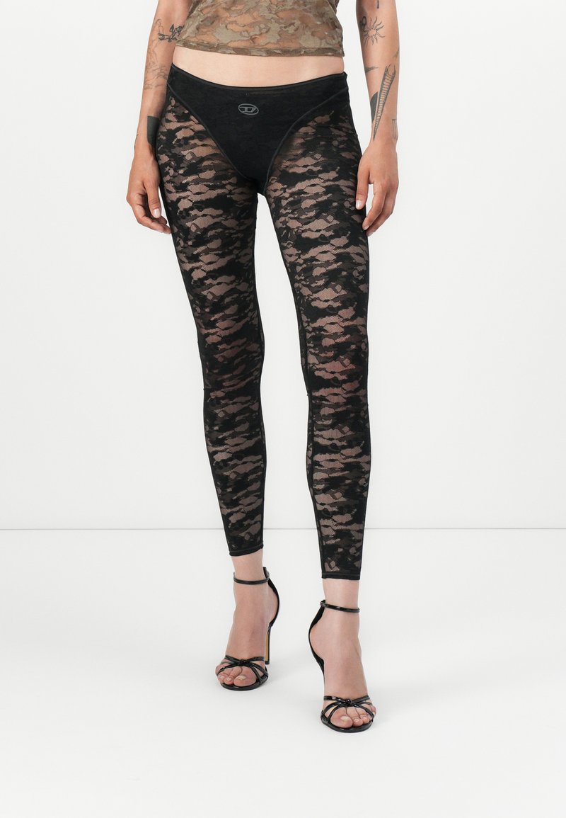 Leggings in pizzo nero con un motivo floreale, vita elastica e design aderente, abbinate a sandali neri con tacco alto e fasce.
