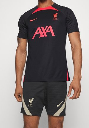Maillot d'entraînement noir et rouge du Liverpool FC avec le logo AXA et short noir arborant les logos de Liverpool et Nike porté par un modèle masculin.