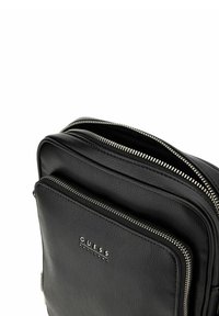 Borsa nera in pelle con esterno strutturato, doppio scomparto con cerniera e piastra con logo argentata sul davanti. Design compatto e rettangolare.