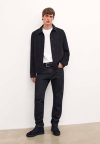 Melnas ādas jaka uzklāta pār balto T-kreklu, apvienota ar tumšiem džinsu biksēm un tumši zilām kurpēm. Gluda tekstūra, pieguļošs dizains, minimālas detaļas.