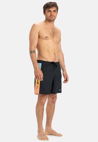 Schwarze Schwimmshorts mit Kordelzug, die ein seitliches Panel in Orange und Blau mit grafischen Akzenten aufweisen. Hergestellt aus leichtem, schnell trocknendem Material.