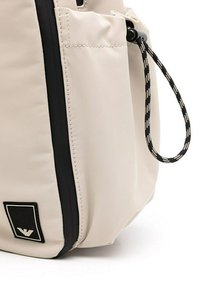 Borsa in tessuto beige con zip nera e dettagli neri, dotata di tasca laterale e cordino con motivo bianco e nero. Patch del logo in evidenza.