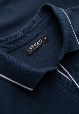 Marine polo t-shirt i struktureret stof, med krave og hvide kontraststriber på kraven. Mærket siger "ombre quintessence."
