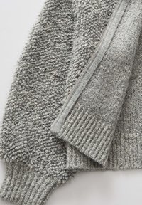 Maglione grigio con zip, realizzato in un tessuto testurizzato e fluffy, con polsini e orlo a coste. La cerniera è ben visibile lungo un lato per la chiusura.