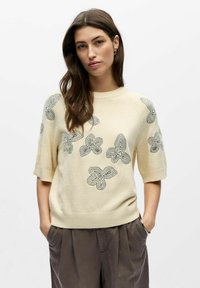 Pull crème à manches courtes avec ourlet côtelé, présentant des motifs de papillons brodés en gris sur toute la partie avant.