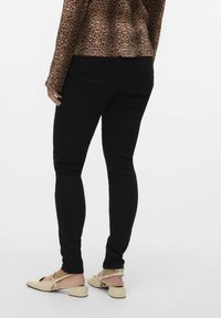 Jeans skinny de mezclilla negra con una textura suave, que presentan bolsillos traseros y un diseño ajustado. Combinados con zapatos de tacón bajo de color claro.
