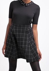 Black short-sleeve top with a decorative collar and a black-and-white checkered skirt. The skirt has a flared design and textured fabric.