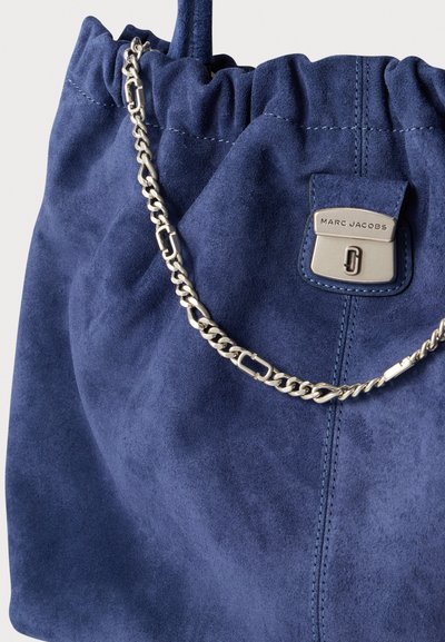 Marineblauwe suède handtas met een geplooide bovenkant, zilveren kettingriem en logoplaatje. Heeft een zachte textuur en minimale stikdetails.