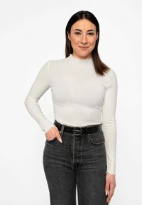 Top bianco a maniche lunghe con collo scallop, abbinato a jeans neri a vita alta e una cintura nera con fibbia rotonda.