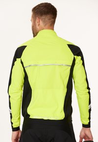 Ljusstark neon-gul och svart jacka med reflexdetaljer, som har en blixtlåsförsedd bakficka och elastiska manschetter. Lätt och ventilerande material.