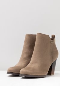 Brązowe botki zamszowe o gładkiej fakturze, zaokrąglonym nosku i średnim słupkowym obcasie. Posiadają małą pętelkę z tyłu ułatwiającą zakładanie.