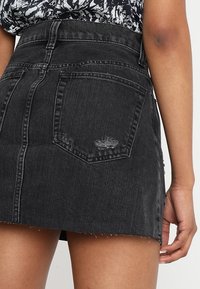 Vista posteriore di una persona che indossa una mini gonna di jeans nera e strappata con orlo a intaglio e un top a motivo bianco e nero.