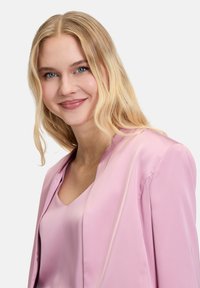 Roze satijnen jas met een gladde afwerking en subtiele glans, voorzien van een ronde kraag en een open voorkant, gedragen over een bijpassend topje.
