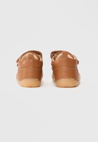 Scarpe in pelle marrone con una finitura morbida e testurizzata, dotate di una fascia sul retro e suole in gomma flessibili. Design semplice con accenti minimalisti.