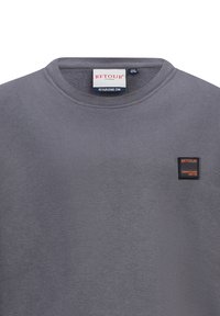 Felpa grigia in misto cotone, con scollo a giro e una piccola toppa rettangolare nera e arancione sul lato sinistro del petto.