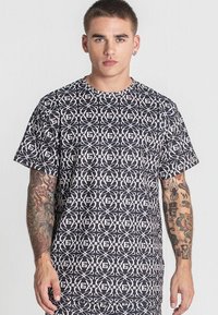 Čierne a biele tričko s geometrickými vzormi, krátkymi rukávmi, klasickým výstrihom a voľným strihom. Materiál sa zdá byť hladký.