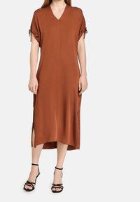 Brown, knee-length dress with a V-neck and short sleeves, featuring side slits and gathered details at the sleeves. Paired with black strappy sandals.