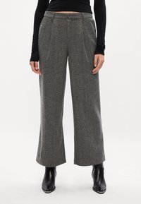 Calças largas de risca de giz cinzentas com cintura alta e pregas frontais, feitas de tecido texturizado; combinadas com botas de tornozelo pretas.