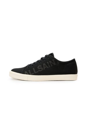 Black canvas sneakers with a cream-colored rubber sole, featuring black eyelets and laces, and a subtle logo printed on the side.