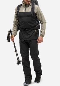 Veste extérieure noire et grise avec fermeture éclair à l'avant, bandes ajustables et texture douce. Pantalons noirs et bâton de trekking avec une poignée en liège.