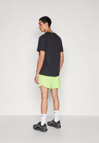 Μαύρο πουκάμισο με κοντά μανίκια, συνδυασμένο με αθλητικό σορτς σε νέον πράσινο χρώμα. Διαθέτει απλό σχέδιο με στρογγυλή λαιμόκοψη και άνετη εφαρμογή.