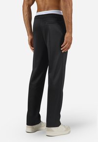 Black sweatpants with a white elastic waistband, featuring a back pocket and a straight-leg design. Smooth fabric and minimal seams.