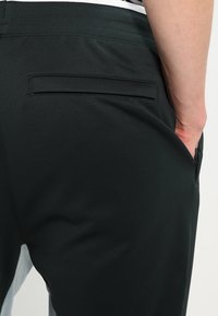 Svarta texturerade byxor med en slät yta, som har en bakficka och resårmidja. Inga synliga logotyper eller mönster.