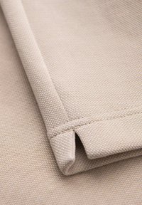 Textil beige con una superficie texturada, que presenta bordes doblados y costuras visibles. Color claro con un patrón simple y uniforme.