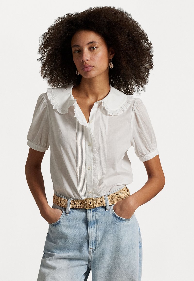 Hvit kortermet bluse med volangkrage, teksturert frontplacket og knapper. Kombinert med lyseblå denim og et vevd belte.