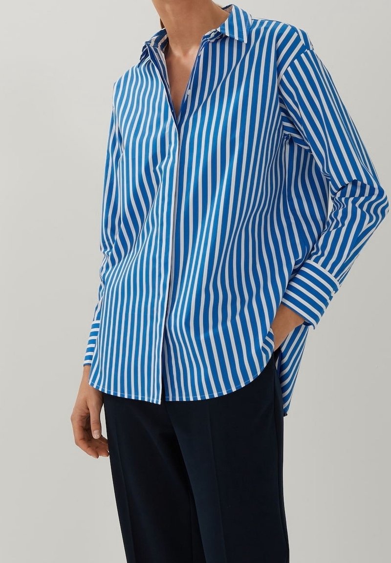 Blå och vit vertikalt randig skjorta med knappar, som har en spetskrage och långa ärmar, med en avslappnad passform och rundad nederkant.
