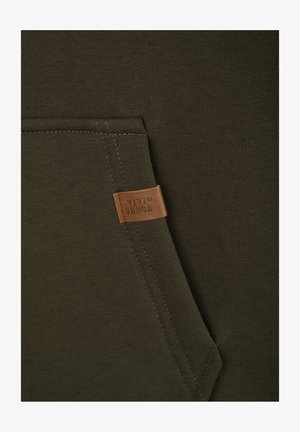 Bluza w kolorze oliwkowej zieleni z prążkowaną fakturą, wyposażona w kieszeń kangurkę oraz beżową skórzaną metkę z wytłoczonym logo.