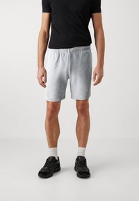 Hellblaue Shorts mit elastischem Bund, geradem Schnitt und Seitentaschen, kombiniert mit einem schwarzen T-Shirt und schwarzen Sportschuhen.