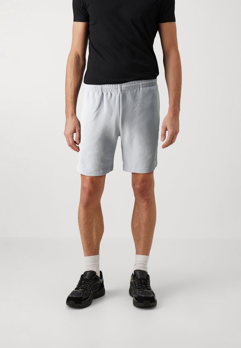 Hellblaue Shorts mit elastischem Bund, geradem Schnitt und Seitentaschen, kombiniert mit einem schwarzen T-Shirt und schwarzen Sportschuhen.