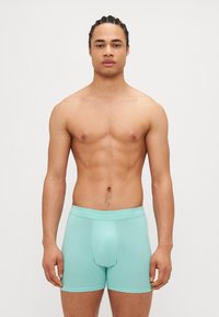 Boxeri din bumbac de culoare azul deschis, cu o ajustare strânsă și bandă elastică pe talie, având logo-ul Calvin Klein. Textură netedă și lungime până la mijlocul coapsei.
