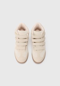 Μπεζ ψηλές αθλητικές κάλτσες με τρεις ιμάντες Velcro και περφορέ λεπτομέρειες, εμφανιζόμενες από πάνω σε λευκό φόντο.