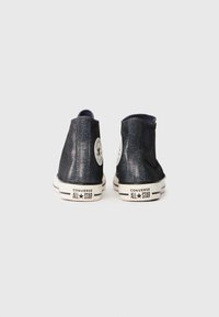 Tenisi înalți negri cu sclipici de la Converse, cu tălpi albe din cauciuc, cusături contrastante în alb și negru și logo-ul iconic cu stea pe toc.