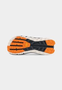 Σόλα παπουτσιού τρεξίματος σε μονοπάτι με βαθιά σχέδια σε πορτοκαλί, μαύρο και λευκό, σχεδιασμένη για κράτημα και ανθεκτικότητα σε τραχύ έδαφος.