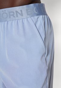 Calções azul claro feitos de tecido macio, com uma cintura larga e a marca "BÖRN" em relevo, além de bolsos laterais. Textura suave e ajuste relaxado.