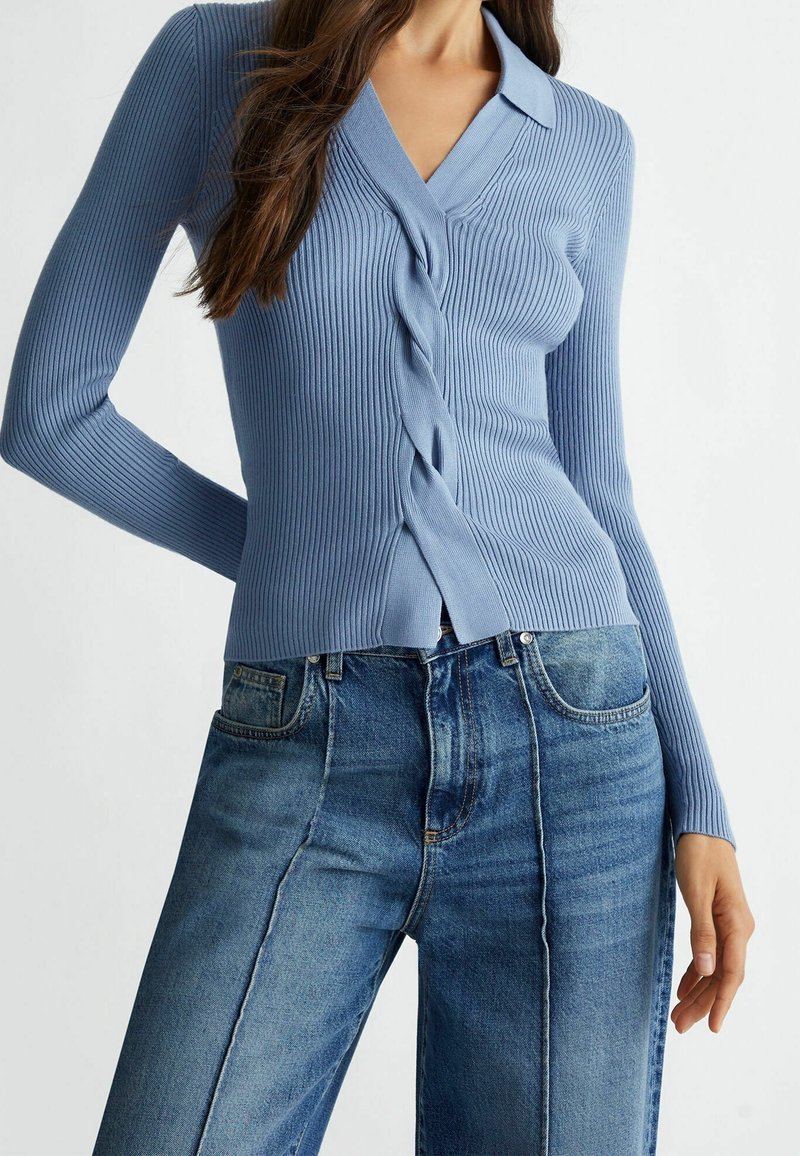 Ljust blå ribbad stickad cardigan med V-ringning och framknäppning, med en vriden design och långa ärmar, ihopkopplad med högmidjade blå jeans.