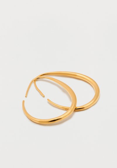 Ζευγάρι λεία, μεσαίου μεγέθους χρυσά κρίκοι σκουλαρίκια με λεπτό, κυρτό κούμπωμα που βρίσκεται πάνω σε λευκή επιφάνεια.