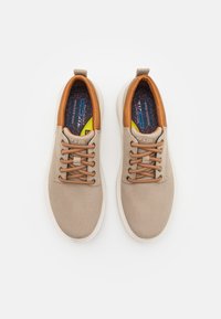 Zapatillas de lona beige con detalles en piel marrón, puntera redonda y cordones marrones en contraste. Superficie suave y texturizada con plantilla acolchada.