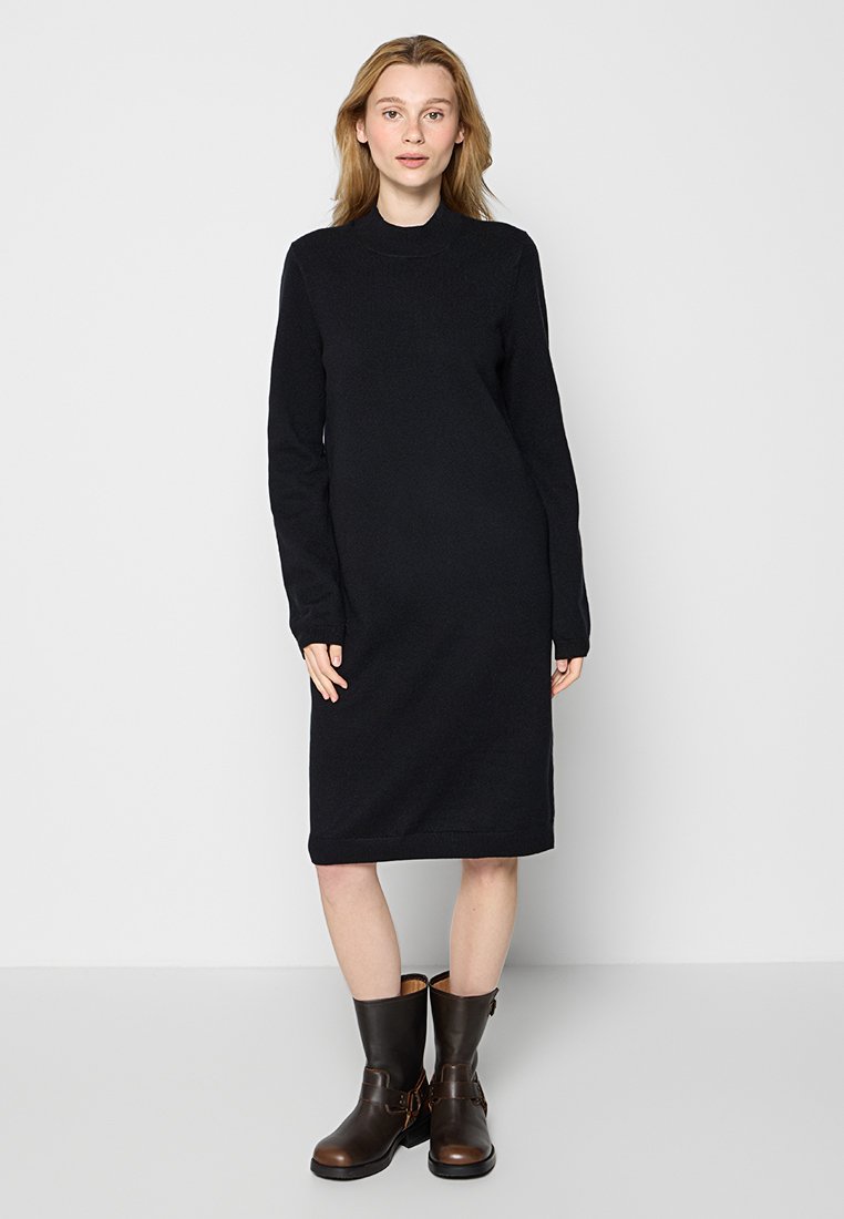 Czarna dzianinowa sukienka z długimi rękawami i wysokim dekoltem, sięgająca do połowy łydki. W zestawieniu z brązowymi botkami za kostkę z akcentami w postaci klamr.