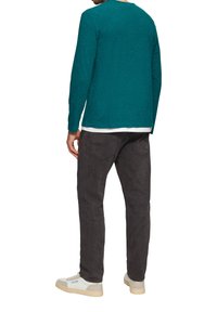 Turkusowa koszula z długimi rękawami o speckowanej fakturze, w parze z ciemnoszarymi spodniami. Buty są białe z brązową podeszwą, z logo na boku.