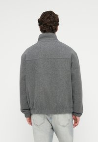 Graue Fleecejacke mit hohem Kragen, elastischem Bund und langen Ärmeln. Einfaches Design mit glatter Textur und minimalen Nähdetails.