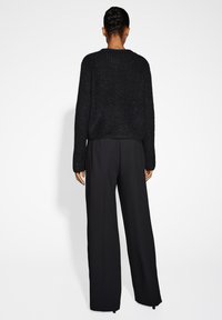 Schwarzer, strukturierten Strickpullover mit langen Ärmeln und rundem Ausschnitt, kombiniert mit lockeren, schwarzen, weit geschnittenen Hosen. Schlichtes Design.