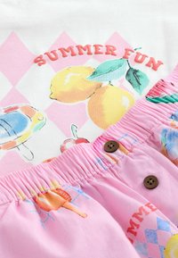 Roze kledingstuk met opdruk van gele citroenen, groene bladeren, kleurrijke ijslollies en de tekst "SUMMER FUN" op een roze achtergrond met diamantpatroon.