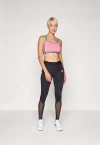 Rosa trenings-BH med turkise stropper, mønstret kant og tre svarte striper. Svarte tights med mesh-detaljer og hvit Adidas-logo.