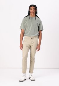 Lys grøn bomulds t-shirt med korte ærmer, parret med beige tapered bukser med elastisk snoreliv og hvide sneakers.