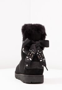 Černé semišové kotníkové boty s límcem z umělé kožešiny, zdobené mašlí a dekorativními rhinestonovými akcenty na podpatku. Gumová podrážka.